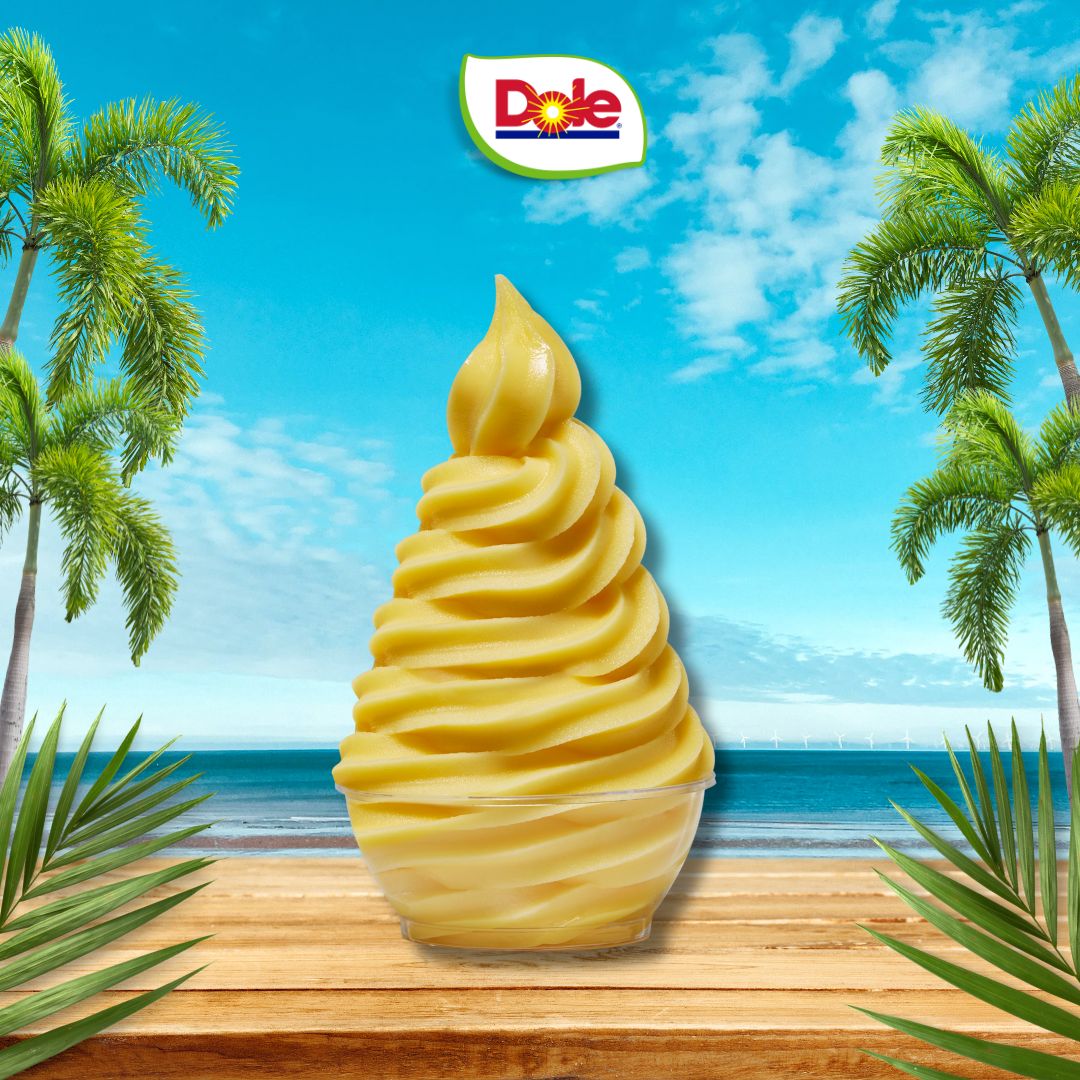 Dole pineapple soft serve ice cream with a tropical background featuring palm trees and a blue sky.